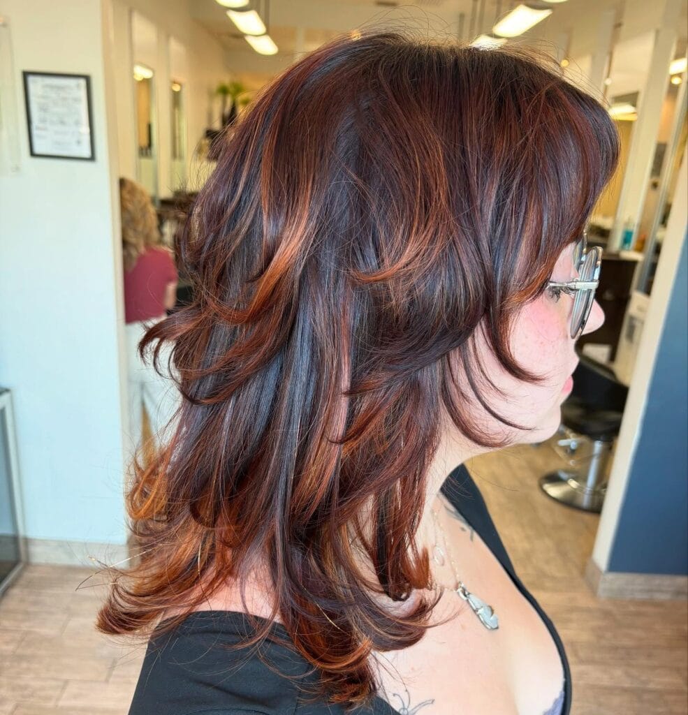 A woman with a medium-length auburn butterfly cut featuring face-framing layers and warm copper highlights.