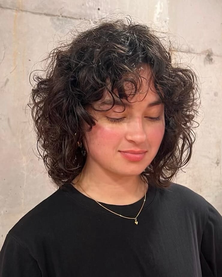 A woman with a dark brown curly shaggy bob featuring face-framing layers and curly bangs.