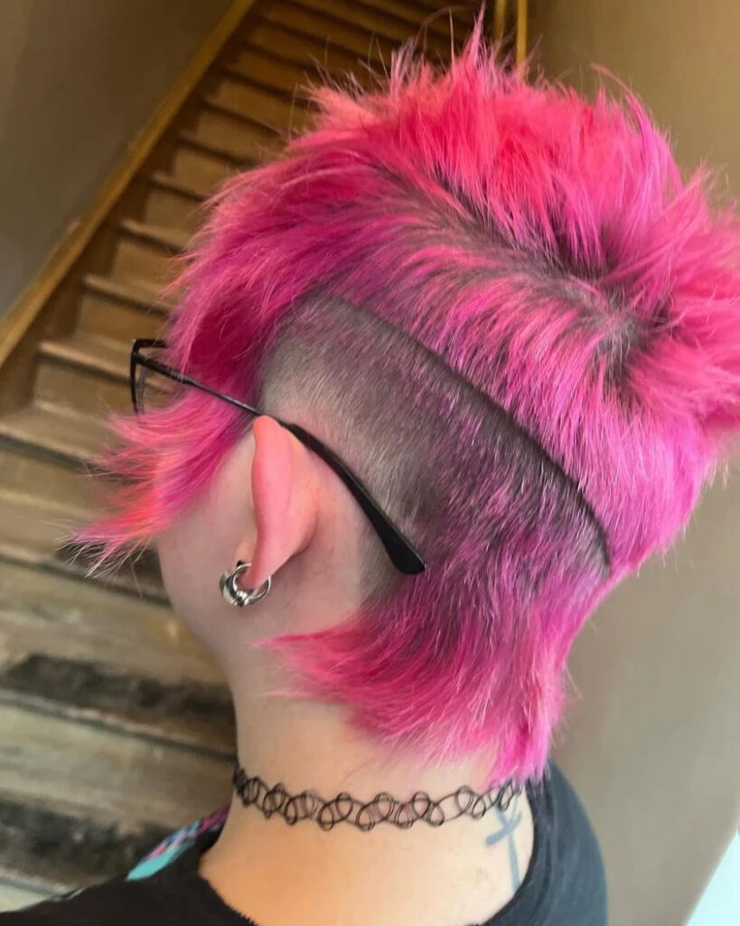 A person with a bright neon pink textured mullet featuring a horizontal shaved undercut above the ear.