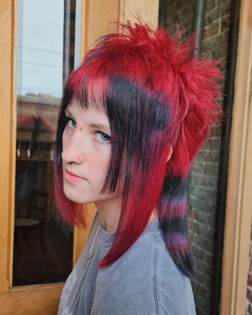 A woman with a spiky red and black shaggy hairstyle featuring horizontal striped raccoon tail patterns on the long side sections.