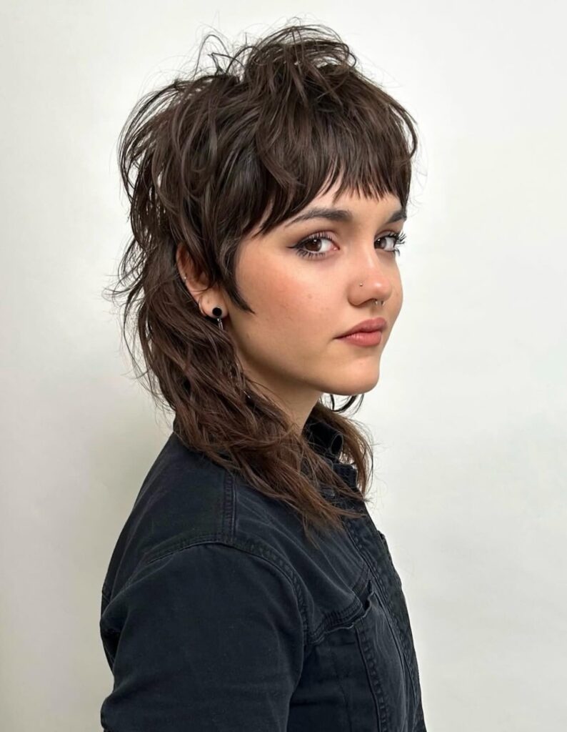 A woman with a messy chocolate brown wolf cut featuring choppy layers and a wispy fringe.