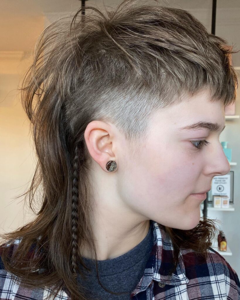 A person with an ash brown punk mullet featuring a high skin fade on the side and a small braid in the long back section.