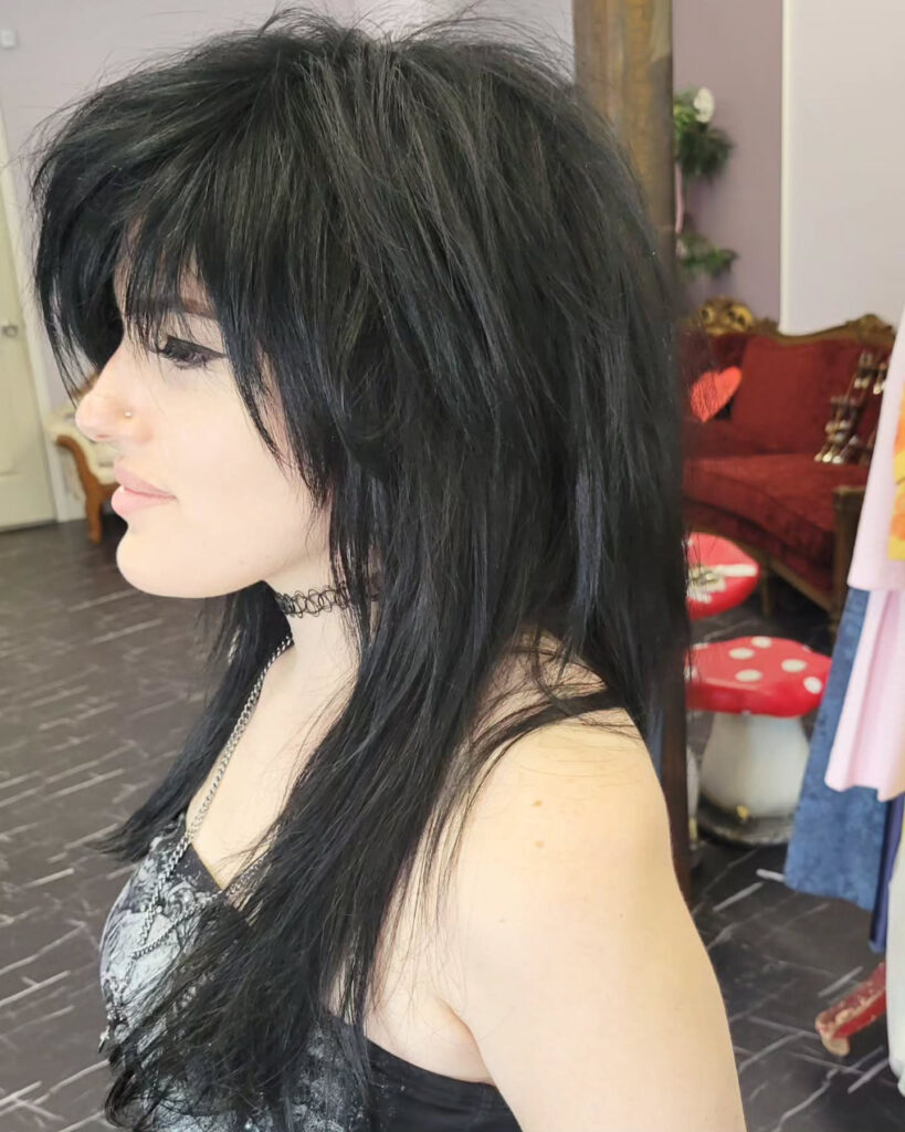 A woman with a long, jet-black, shaggy haircut featuring voluminous choppy layers and a wispy fringe.