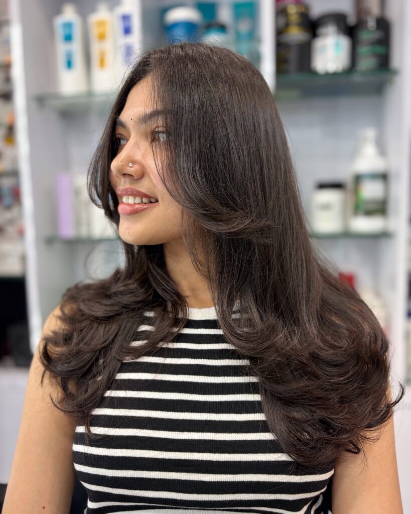 A woman with long, dark brown hair styled in voluminous butterfly layers with flipped-out ends.