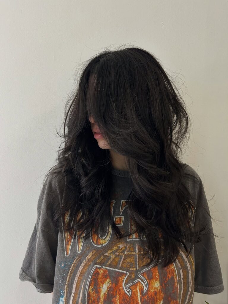 A woman with long dark espresso hair featuring heavily textured layers and long face-covering curtain bangs.