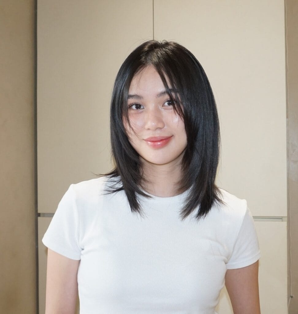 A woman with a straight black medium lob haircut featuring soft face-framing layers and a center part.