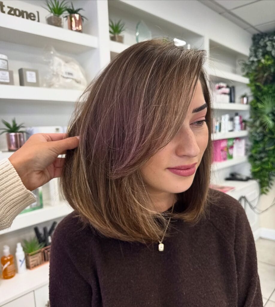 A woman with a voluminous mushroom-brown lob featuring sandy-blonde highlights and a deep side-swept fringe.