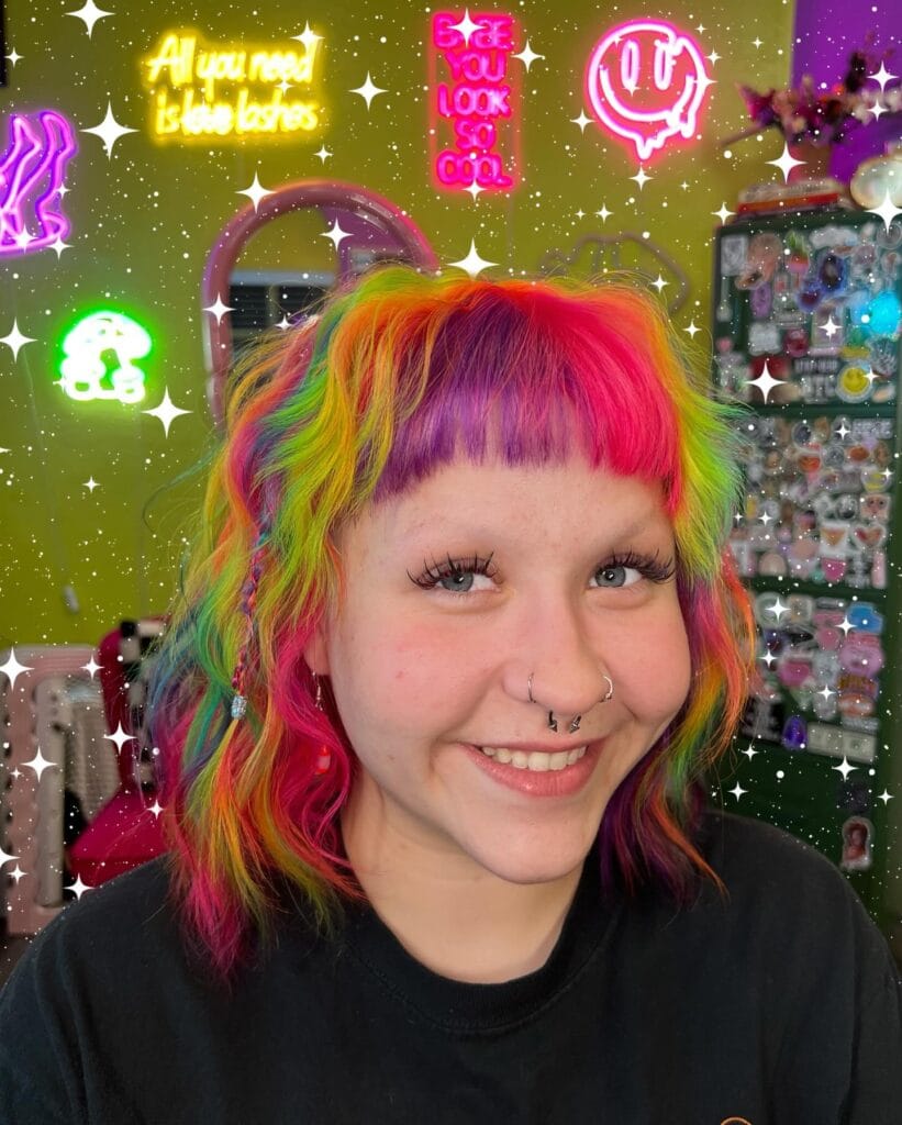 A person with a shoulder-length rainbow-colored lob featuring micro bangs and layered texture.
