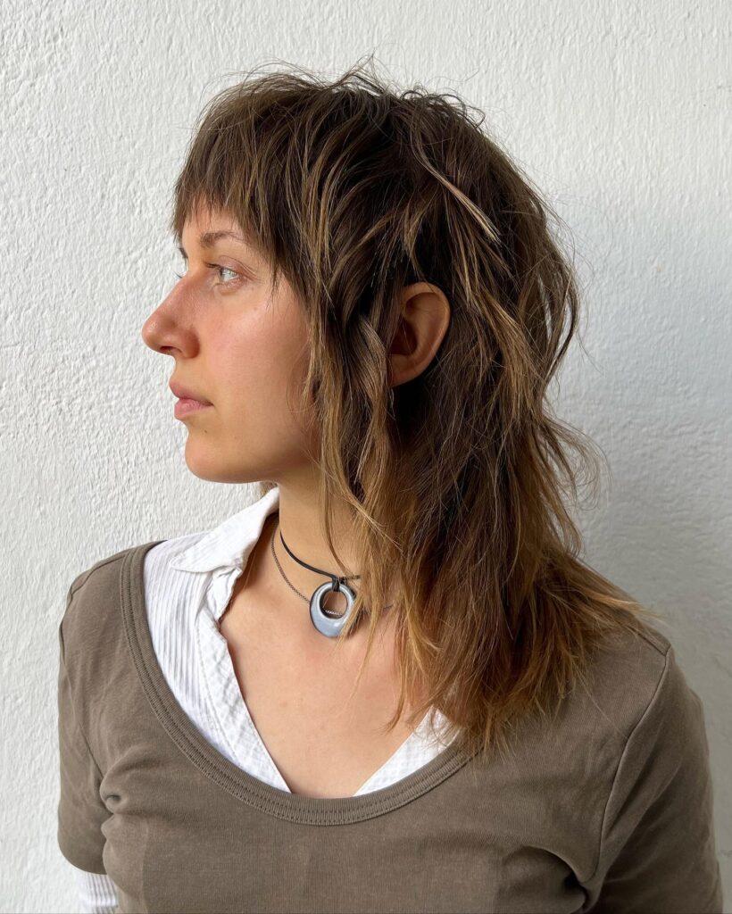 A woman with wavy, layered, rich brown hair featuring subtle highlights and a textured fringe.