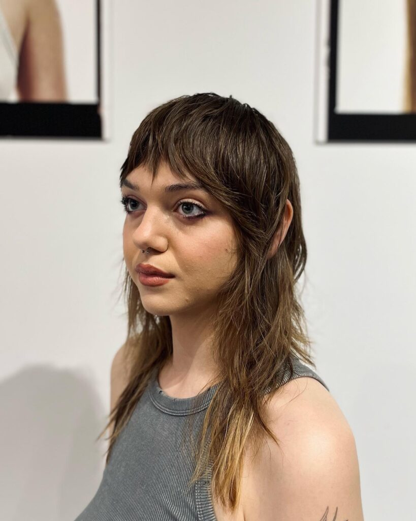A woman with a textured brunette mullet featuring a short choppy fringe and subtle golden highlights on the ends.