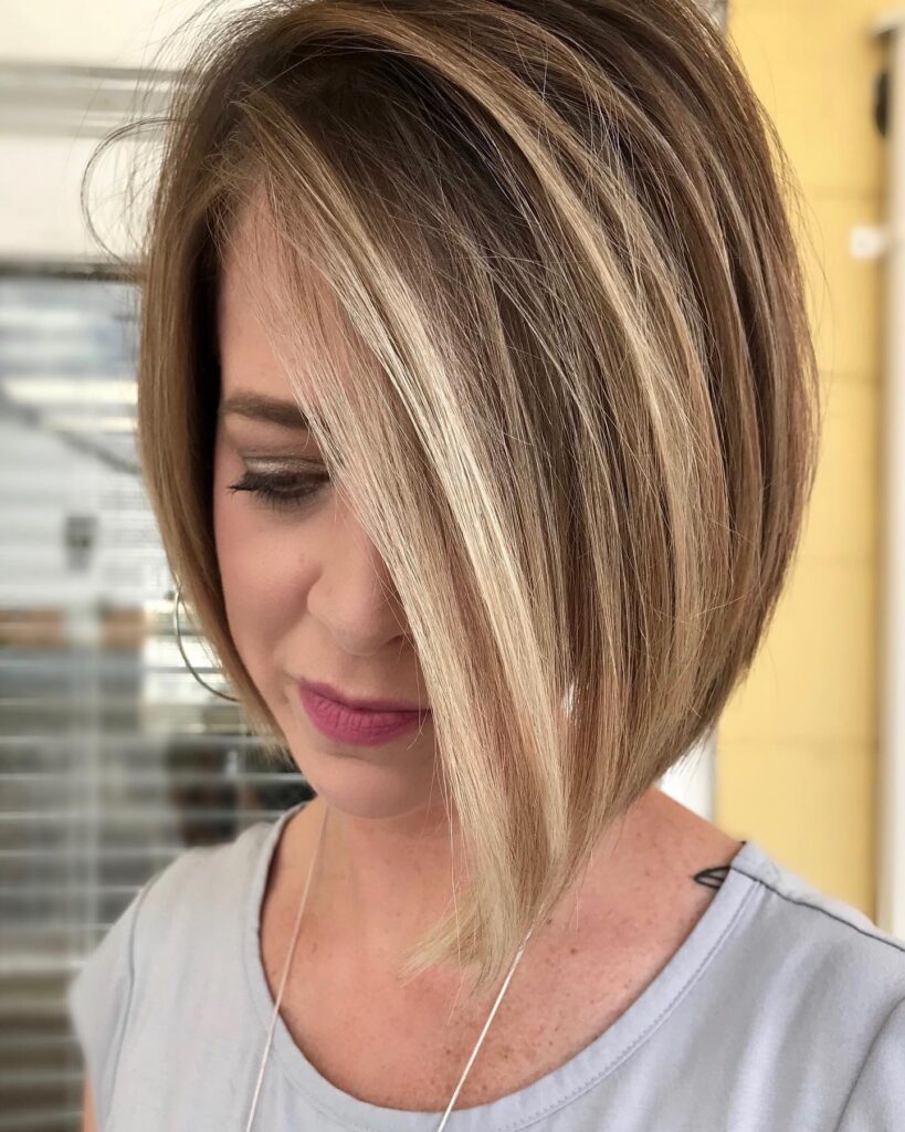 A woman with a sleek asymmetrical bob featuring dimensional blonde highlights over a medium brown base.