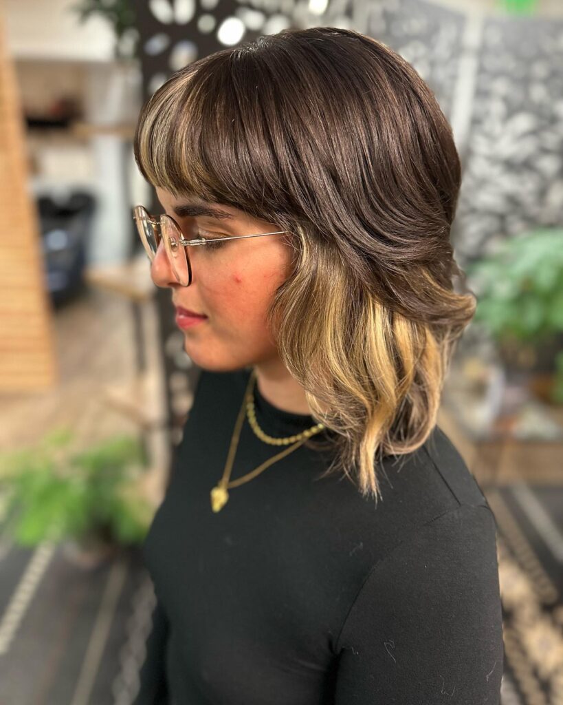 A woman with glossy dark brown hair featuring a full fringe and hidden honey blonde highlights peeking through at the ends.