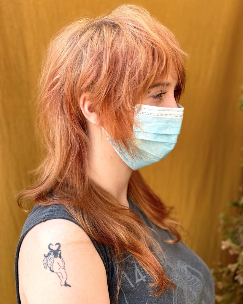A woman with a long, copper-brown, shaggy haircut featuring warm highlights and textured wispy layers.