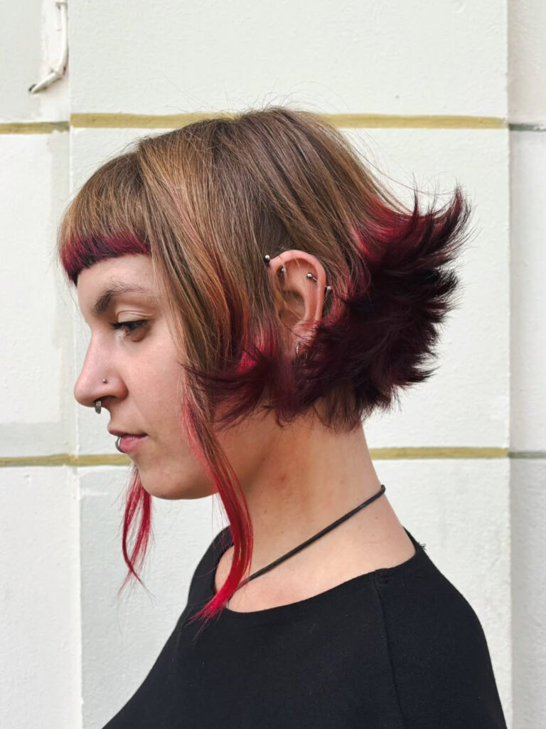 A woman with a short brunette bob featuring a micro fringe and dramatic crimson red flipped ends.