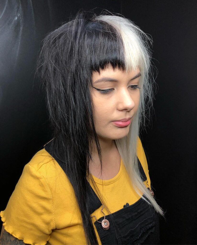 A woman with a medium-length shaggy haircut featuring a black and white split hair color and blunt bangs.