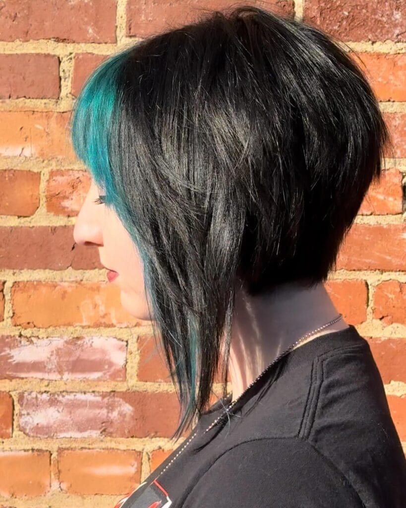 A woman with a sharp asymmetrical black bob featuring a bright teal blue peekaboo fringe.