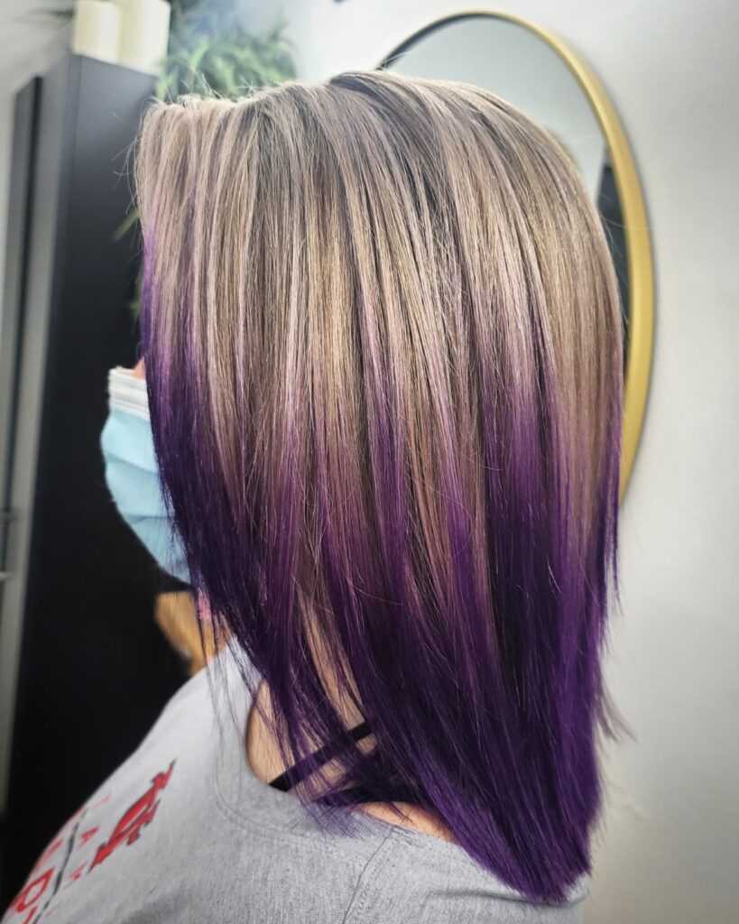 A person with straight mid-length ash blonde hair featuring a vibrant deep purple ombre at the ends.