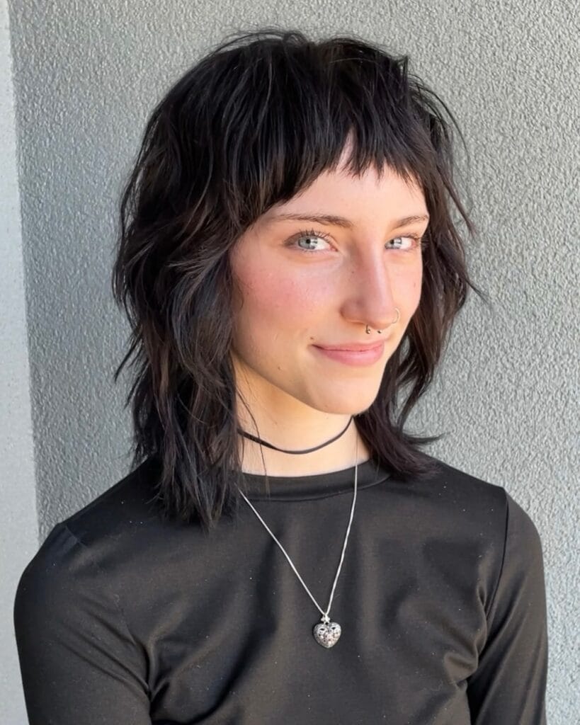 A woman with a black shoulder-length wolf cut featuring choppy layers and edgy micro-bangs.