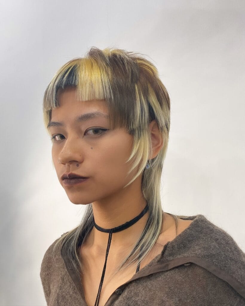 A person with a creative jellyfish haircut featuring blonde and brown block coloring with short top layers and long straight hair underneath.