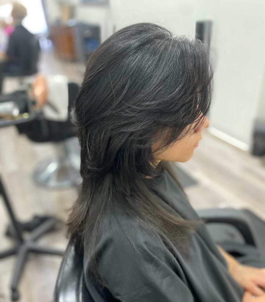 A woman with long black hair in a feathered wolf cut with voluminous layers and side-swept bangs.