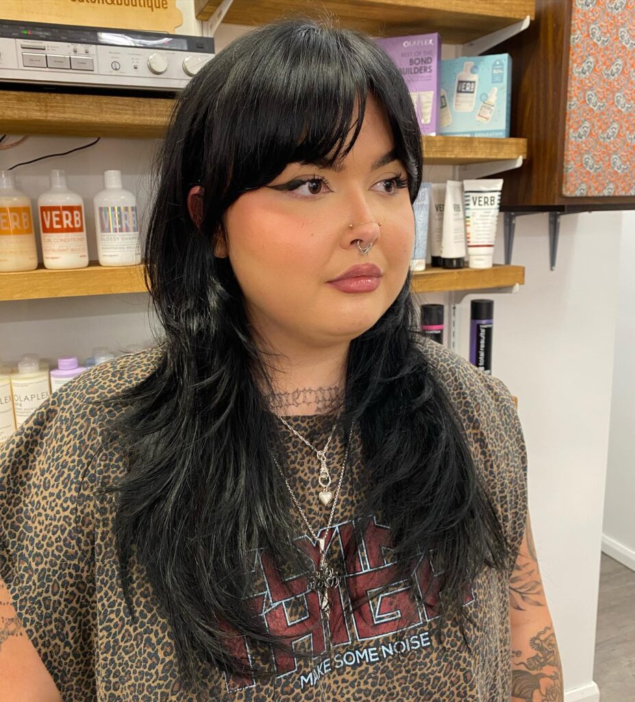 A woman with long, layered black hair and tapered curtain bangs that frame her face.