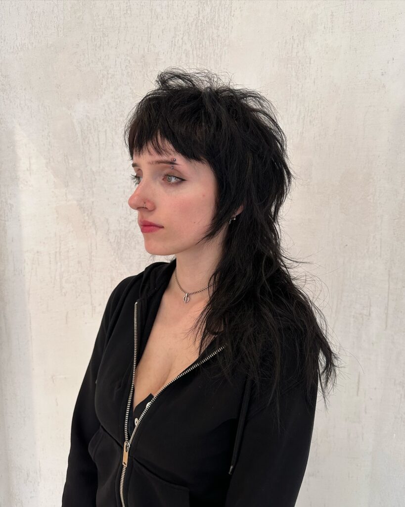 A woman with long black hair in a textured mullet shag with short micro bangs.