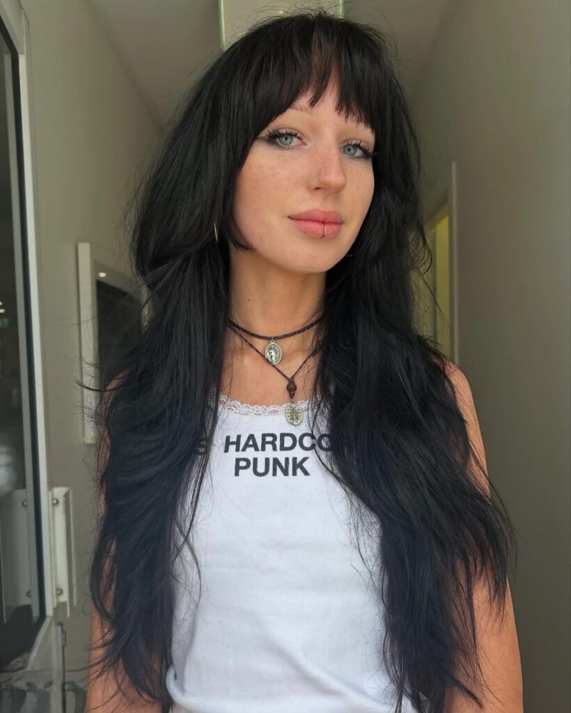 A woman with very long layered black hair and wispy bangs with sharp face-framing side pieces.