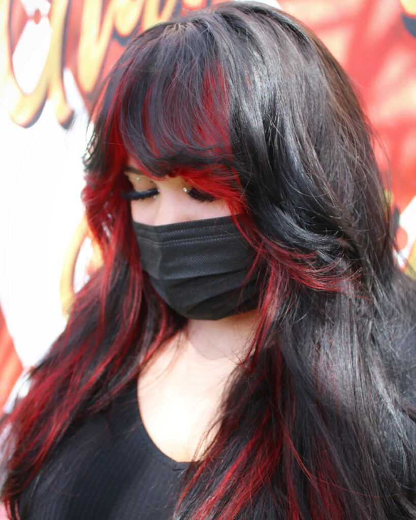 A woman with long black hair featuring bright red peekaboo highlights and a sweeping layered fringe.