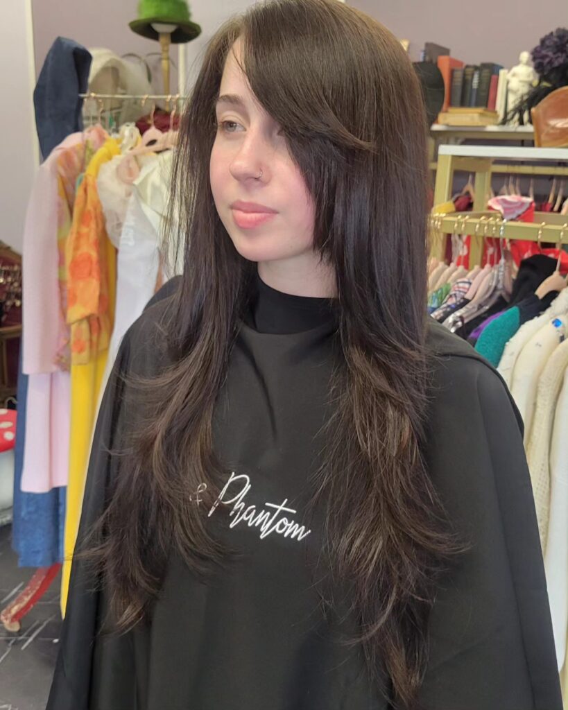 A woman with long straight dark brown hair featuring layered ends and a side-swept fringe.