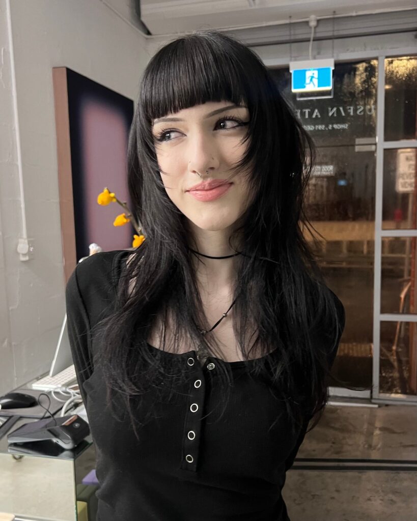 A woman with long, layered black hair and thick, arched bangs that frame her face.