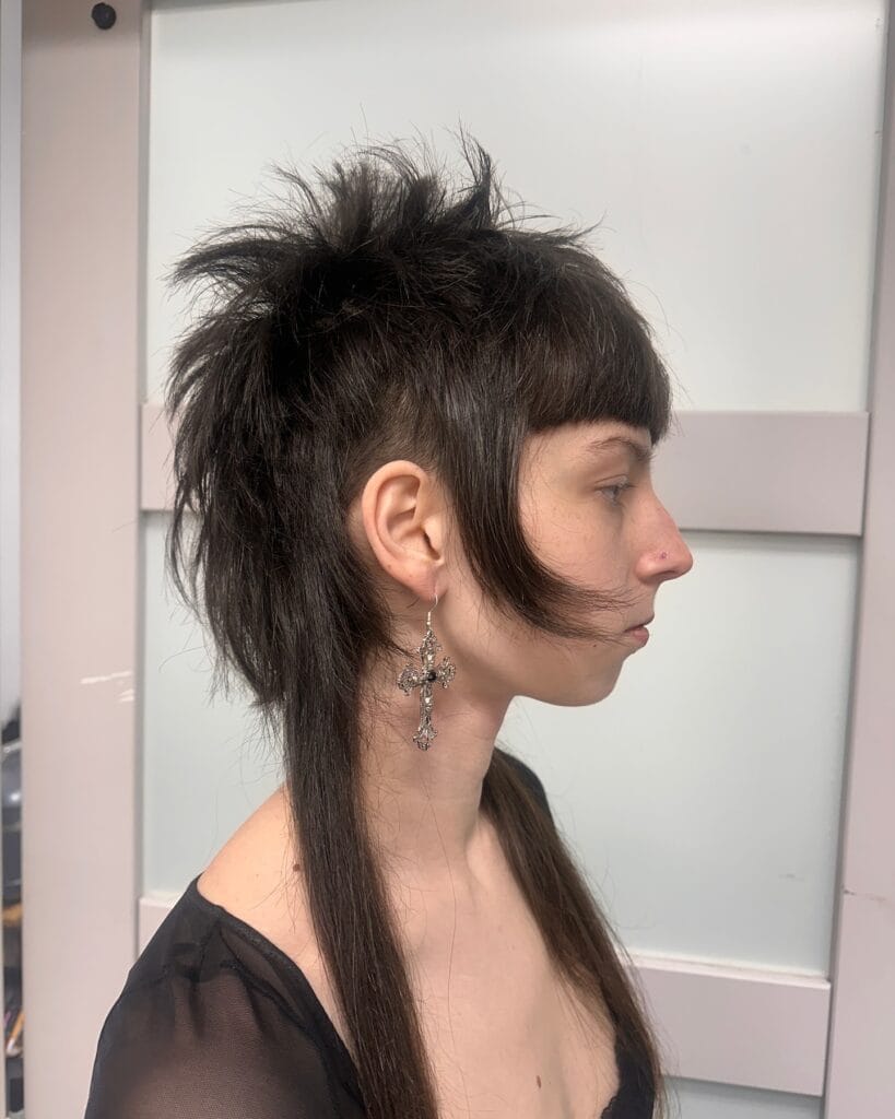 A woman showing off a dark brunette mullet with spiky top layers and long straight hair at the back.