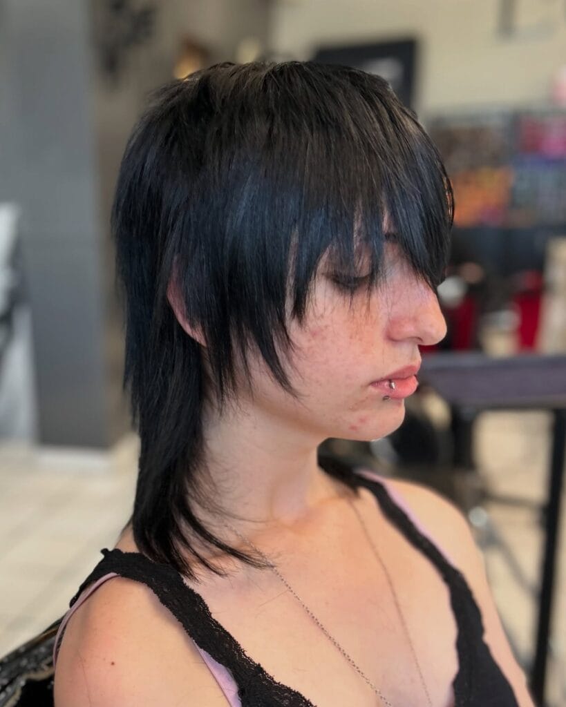 A woman with a sleek jet black shaggy haircut featuring sharp razor layers and a long heavy fringe.