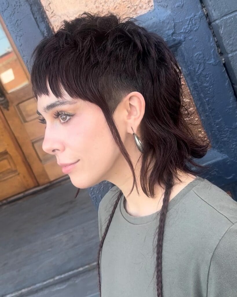 A woman with a dark brunette mullet featuring shaved sides and thin braided accents.