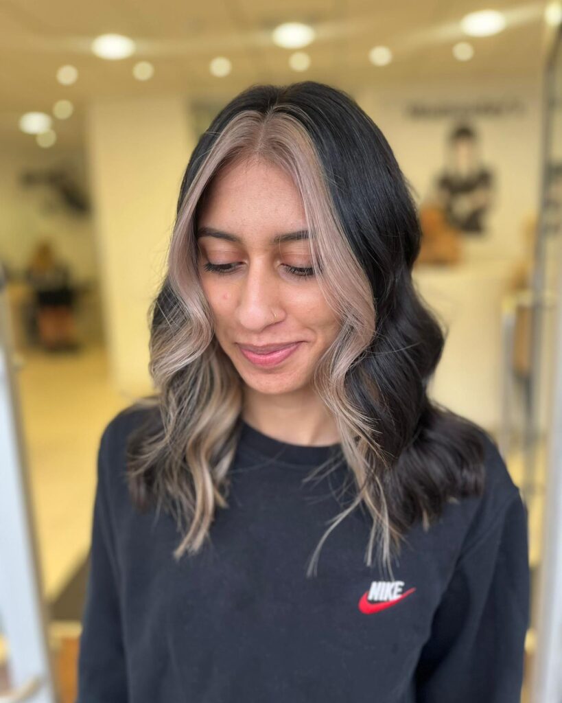A woman with shoulder-length dark wavy hair featuring a cool ashy blonde money piece.