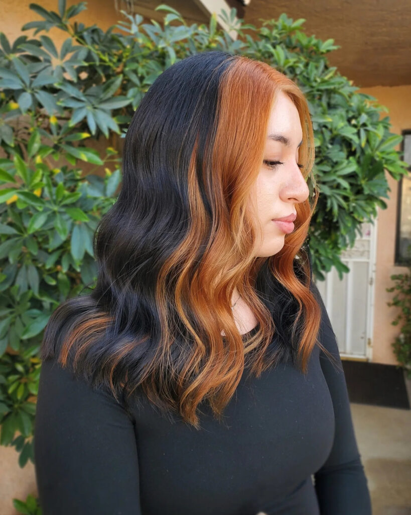 A woman with shoulder-length wavy black hair and a vibrant burnt copper money piece framing her face.