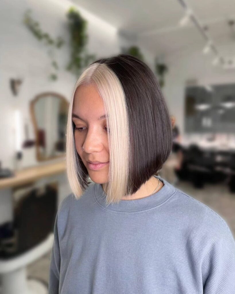 A woman with a sleek dark brown bob and a high-contrast creamy blonde money piece framing her face.