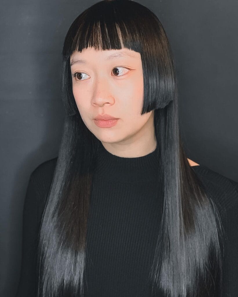 A woman with long straight black hair featuring a blunt micro fringe and sharp cheek-length side sections in a modern hime cut style.