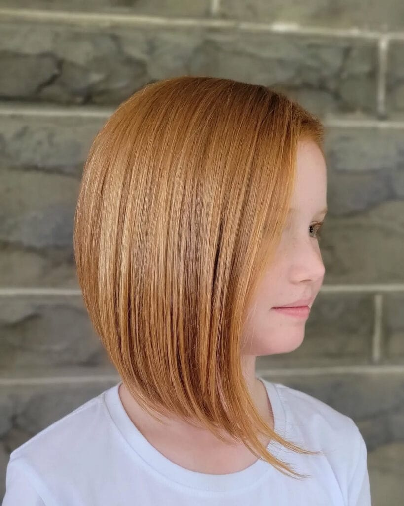 A side profile of a girl with a sleek asymmetrical bob in a bright strawberry blonde shade.