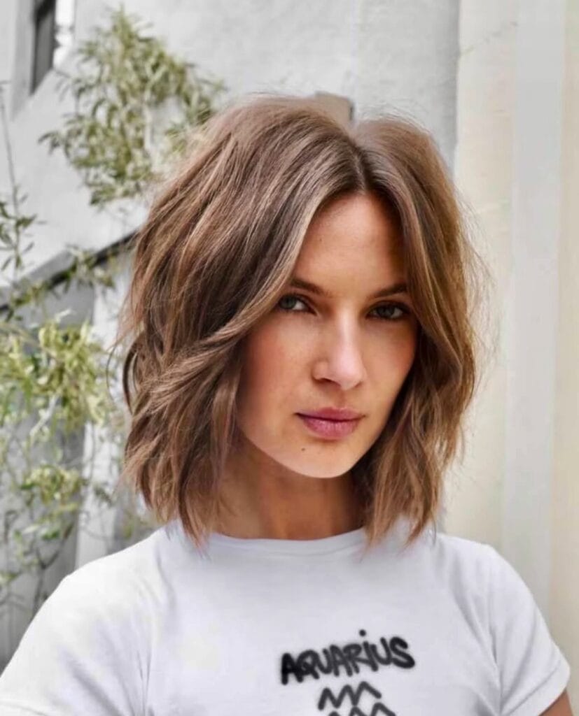 A woman with a mousy brown shaggy lob and a middle part featuring soft, textured waves.