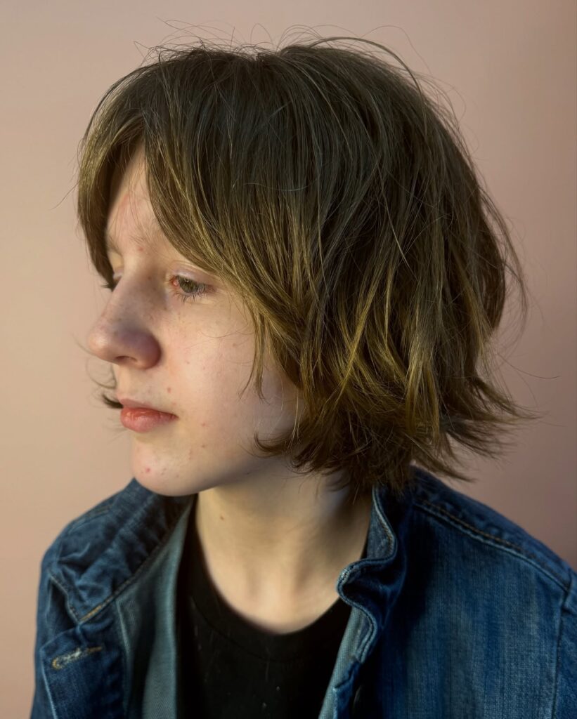 A person in profile with a chin-length shaggy bob featuring messy, textured layers and golden blonde highlights.