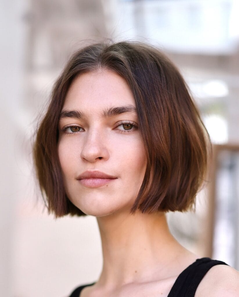 Chin-length blunt bob with a center part and smooth straight texture in a rich brunette shade.