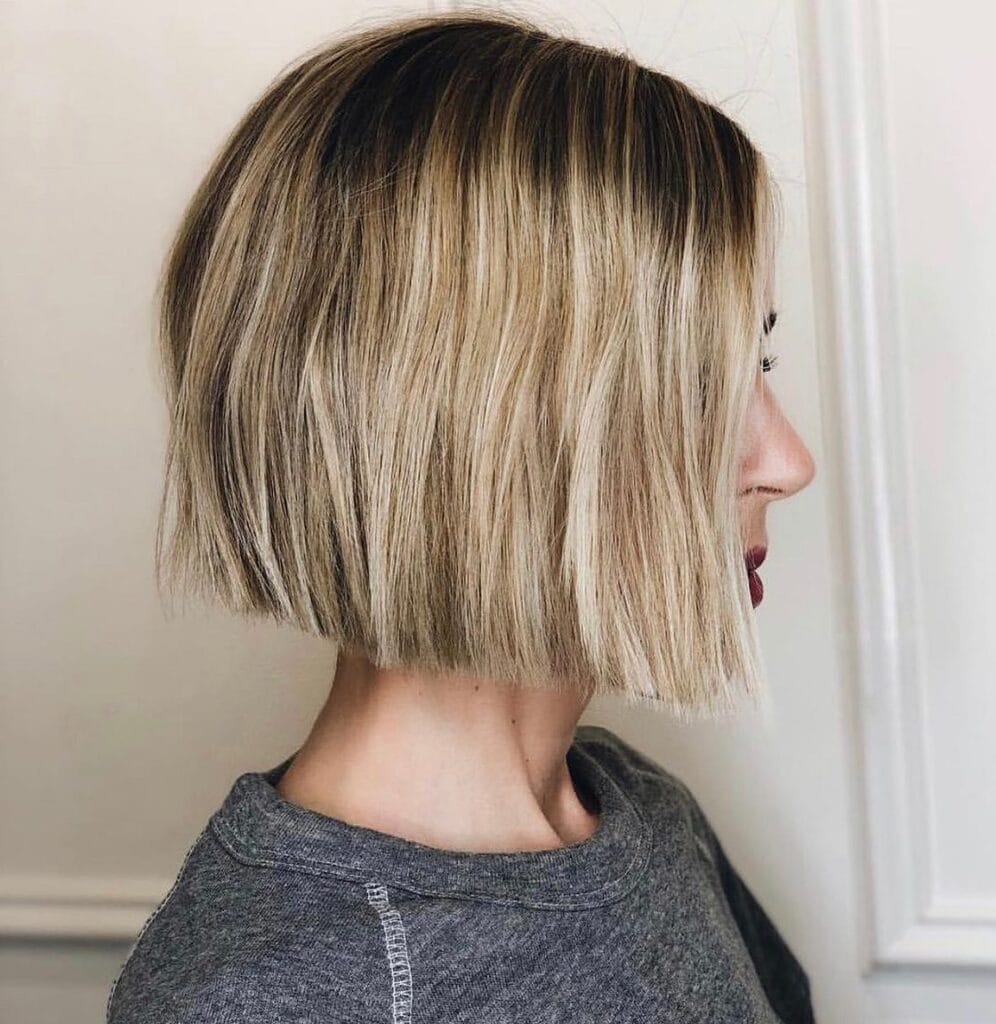 Chin-length blunt bob on straight blonde hair with darker roots and a sleek, slightly angled finish.