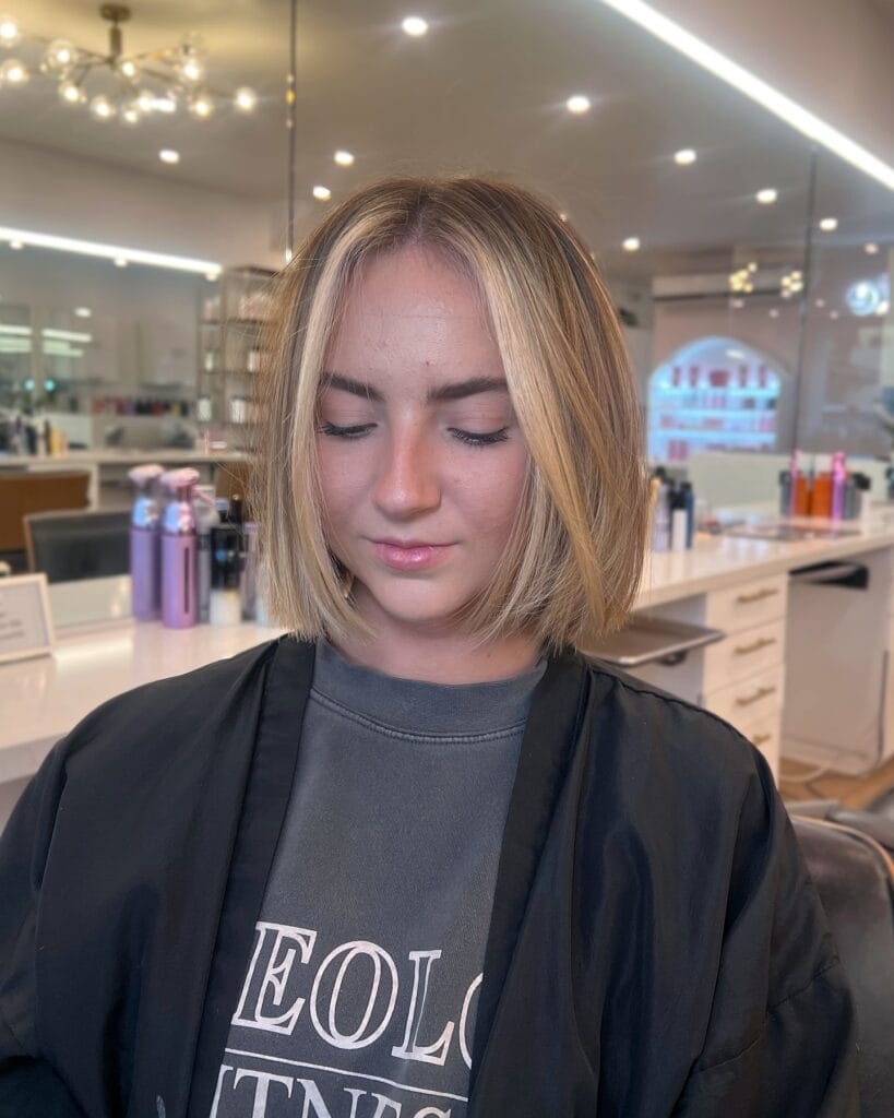 Chin-length blunt bob with a soft center part and bright blonde face-framing highlights that add dimension to the natural sandy blonde base.

