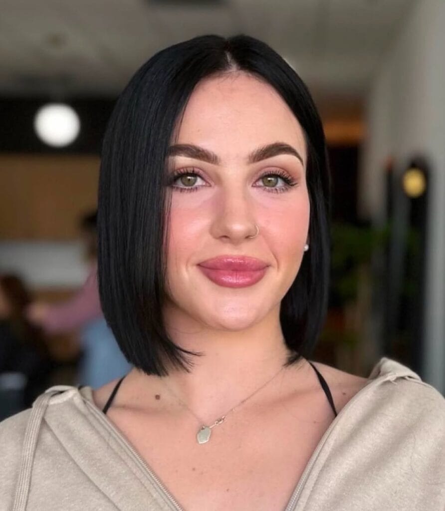 Chin-length straight black bob with a center part and sleek, slightly tucked sides for a smooth, polished look.