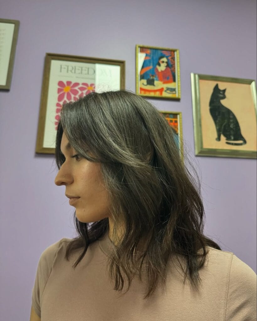 Collarbone-length brunette hair with soft layers and loose natural waves, styled with a subtle off-center part for relaxed movement and texture.