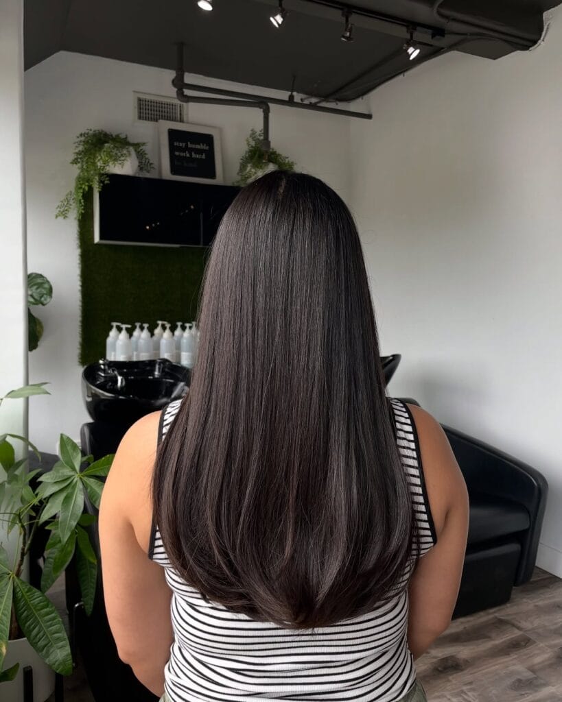 Back view of long, smooth dark brown hair with soft subtle layers and lightly tapered ends, styled sleek and straight to mid-back length.
