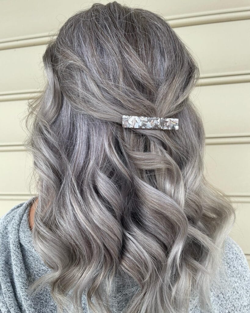 Long layered gray hair styled in loose waves and pinned in a half-up look, highlighting natural white streaks and dimensional silver tones.
