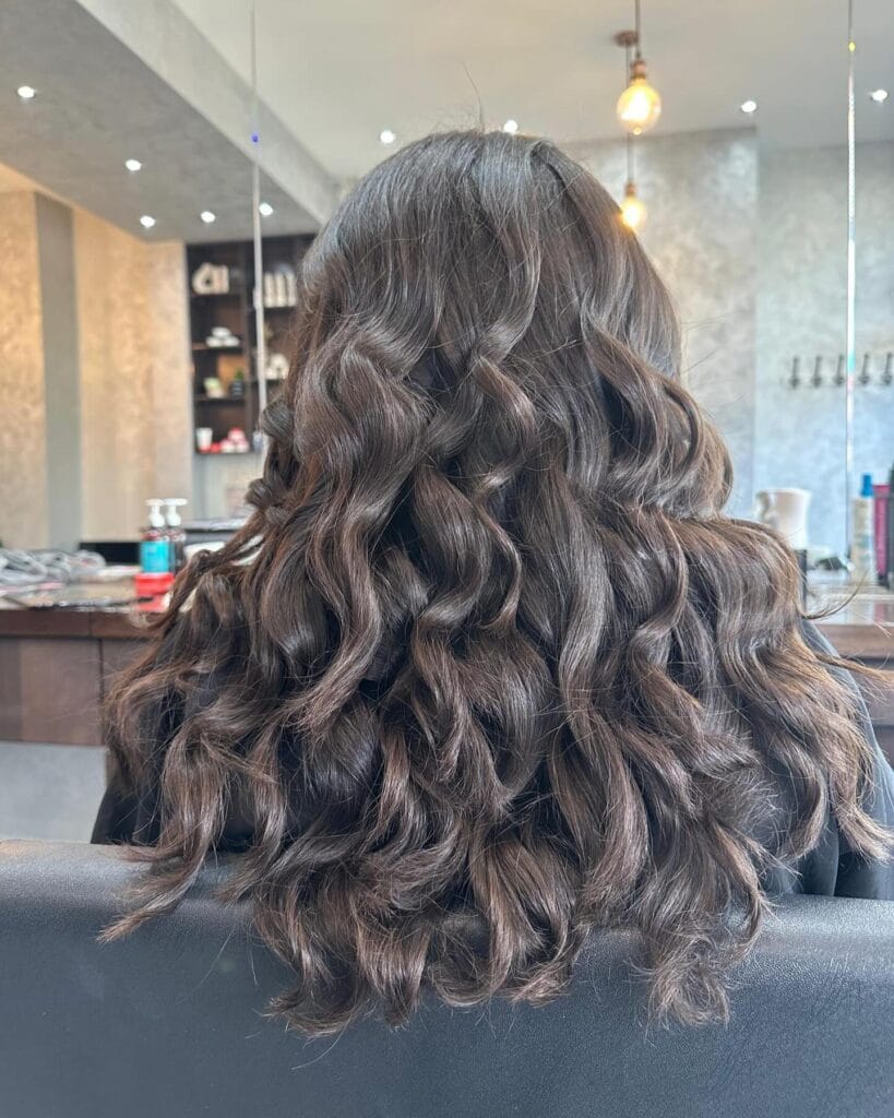 Long dark brunette hair styled with soft, loose curls and layered ends for full, natural volume and movement.