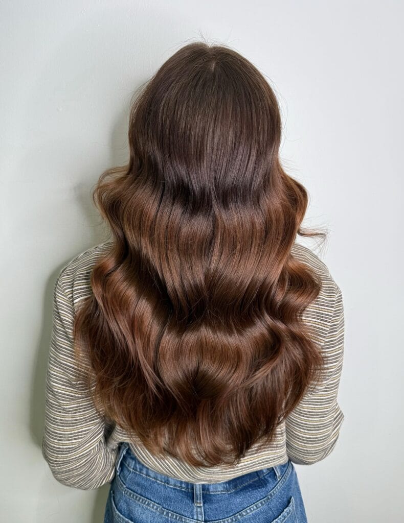 Long layered hairstyle with soft flowing waves and rich chestnut brown tones for smooth movement and shine.