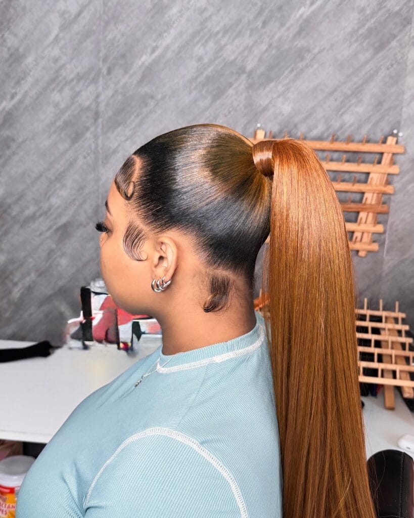 Long straight honey-blonde ponytail styled high and sleek with a wrapped base, smooth glossy finish, and laid baby hairs along the hairline.